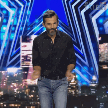 a man in a black shirt and jeans stands on a stage in front of a sign that says got talent on it