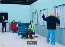 a group of people are sitting in chairs in a room with a man standing in front of a window .