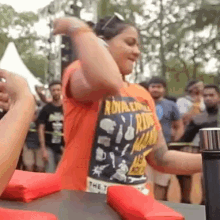 a woman wearing an orange shirt with the word royal on it is standing in front of a crowd .