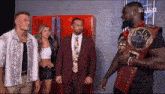 a man in a suit and tie is holding a wrestling championship belt while standing next to two other men