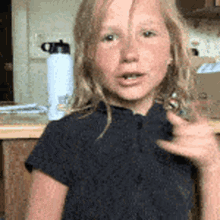 a young girl in a black shirt is sitting at a table with a water bottle in the background .