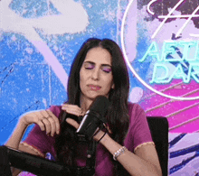 a woman in a purple shirt is sitting in front of a microphone in front of a neon sign that says after dark