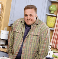 a man wearing a plaid shirt is standing in a kitchen