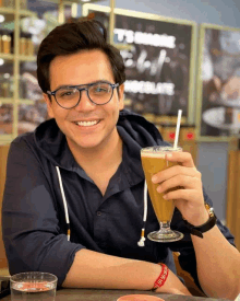 a man wearing glasses is holding a drink in front of a sign that says thank you chocolate