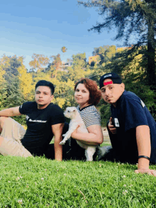 a woman holding a small white dog sits in the grass with two boys