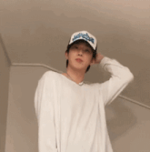 a young man wearing a white sweater and a baseball cap is standing in a room .