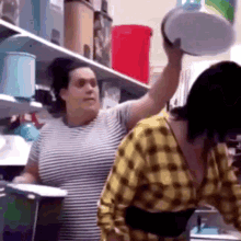 two women are standing next to each other in a kitchen . one woman is holding a bowl over her head .