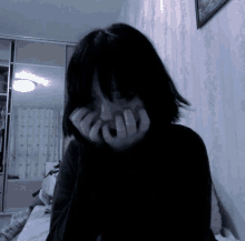 a girl is covering her face with her hands in a dark room