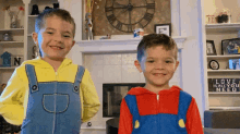 two young boys are standing next to each other in front of a fireplace and a sign that says love is all you need