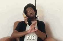 a man is sitting in a chair holding a piece of food and making a no gesture .