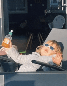 a little girl wearing sunglasses is sitting in a chair holding a bottle of orange juice