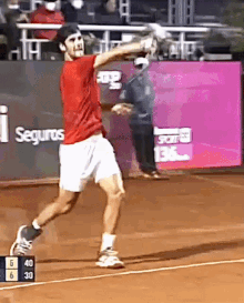 a man in a red shirt and white shorts is swinging a tennis racket on a court with seguros written on the wall