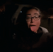 a woman wearing glasses is sticking her tongue out in the dark