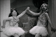 a man and a woman in tutus are dancing together in a black and white photo .