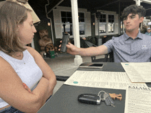 a man is taking a picture of a woman 's cell phone while sitting at a table