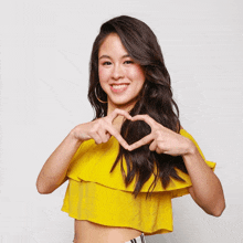 a woman in a yellow top making a heart with her hands