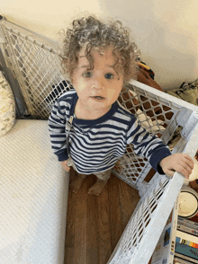 a little boy with curly hair is standing in front of a white plastic gate