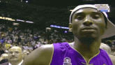 a basketball player wearing a purple jersey and a white hat stands in front of a crowd at a basketball game