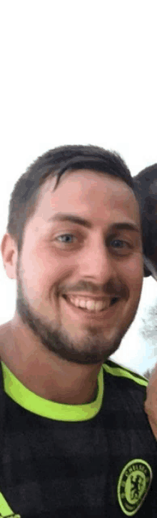 a man with a beard is smiling for the camera while wearing a black and yellow shirt .