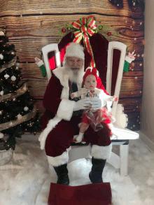 a baby is sitting on santa 's lap in front of a wooden backdrop