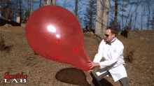 a man in a lab coat is blowing up a red balloon with the words slowmo lab written on the bottom