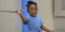 a little girl is wearing a blue dress and pointing at something .