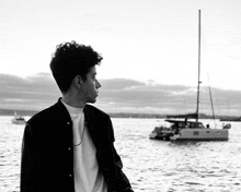 a man stands in front of a body of water with a boat in the background