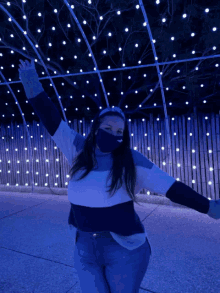 a woman wearing a face mask is standing in front of a fence of lights