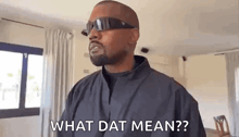 a man wearing sunglasses and a black jacket is standing in a living room and asking what dat mean .