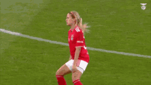 a female soccer player wearing a red jersey with the number 20 on it is standing on a field .