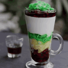 a glass of ice cream with a green swirl on top is on a table next to a shot glass .