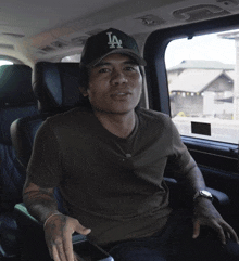 a man sitting in a car wearing a la hat