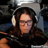 a woman wearing headphones and glasses is sitting in front of a microphone with sweettails written on the bottom right