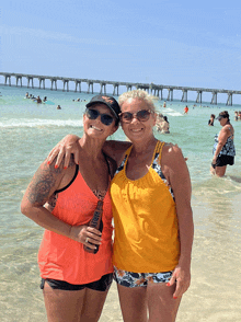 two women posing for a picture on a beach with one wearing a tank top that says ' honey ' on it