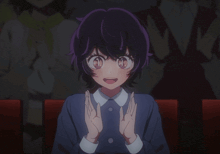 a girl with purple hair is sitting in a theater with her hands up