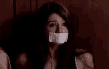 a woman with a piece of tape on her mouth is sitting in a dark room .