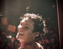 a woman with curly hair is smiling with a crowd in the background