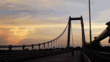 a bridge with a sunset in the background and a person riding a bike