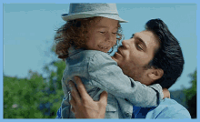 a man is holding a little boy in his arms and the little boy is wearing a hat