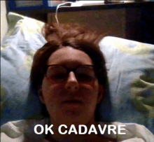 a woman wearing glasses is laying in bed with the words ok cadavre above her