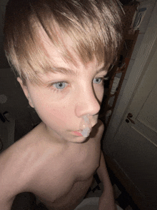 a young boy without a shirt is taking a selfie with a bottle of johnson 's toothpaste behind him