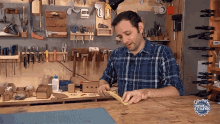 a man in a plaid shirt is working on a piece of wood in a workshop with a sign that says manual de mundo