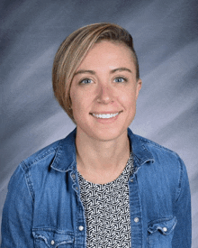 a woman wearing a blue denim shirt and a black and white shirt smiles for the camera