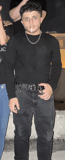 a young man wearing a black shirt and black jeans is smoking