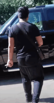 a man in a black shirt is walking towards a black suv