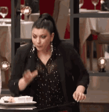 a woman in a black jacket is standing in front of a table with a plate of food on it