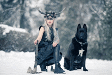 a woman in a horned helmet sits next to a black dog in the snow