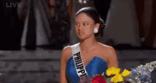 a woman in a blue dress is holding a bouquet of flowers and wearing a sash that says philippine .