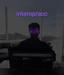 a man sitting in front of a computer with a purple background that says " interop / acc "