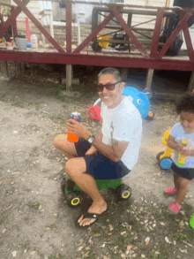 a man sits on a green toy car while a little girl sits next to him